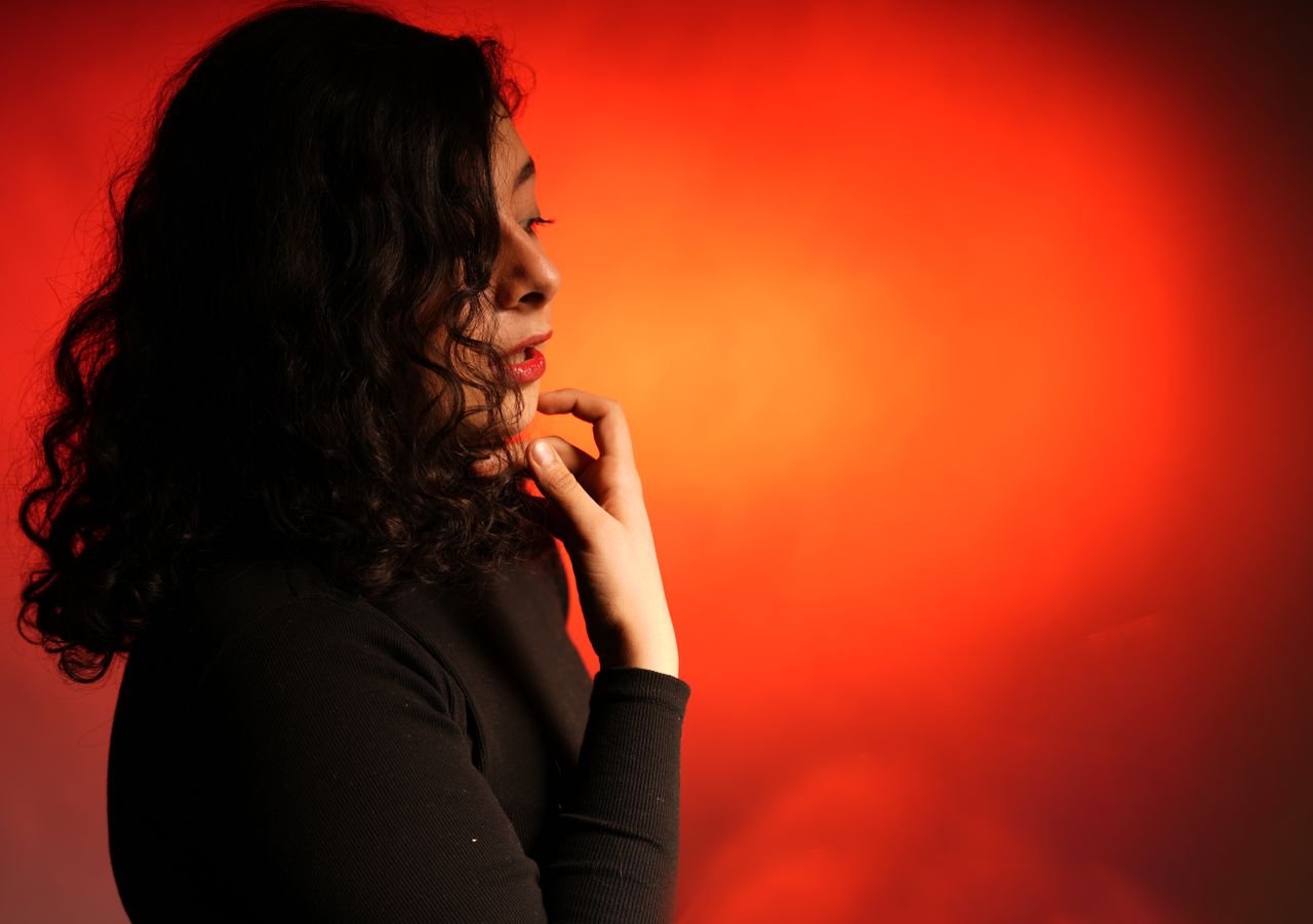 Profile of a woman with curly hair pondering, set against a vivid red backdrop.